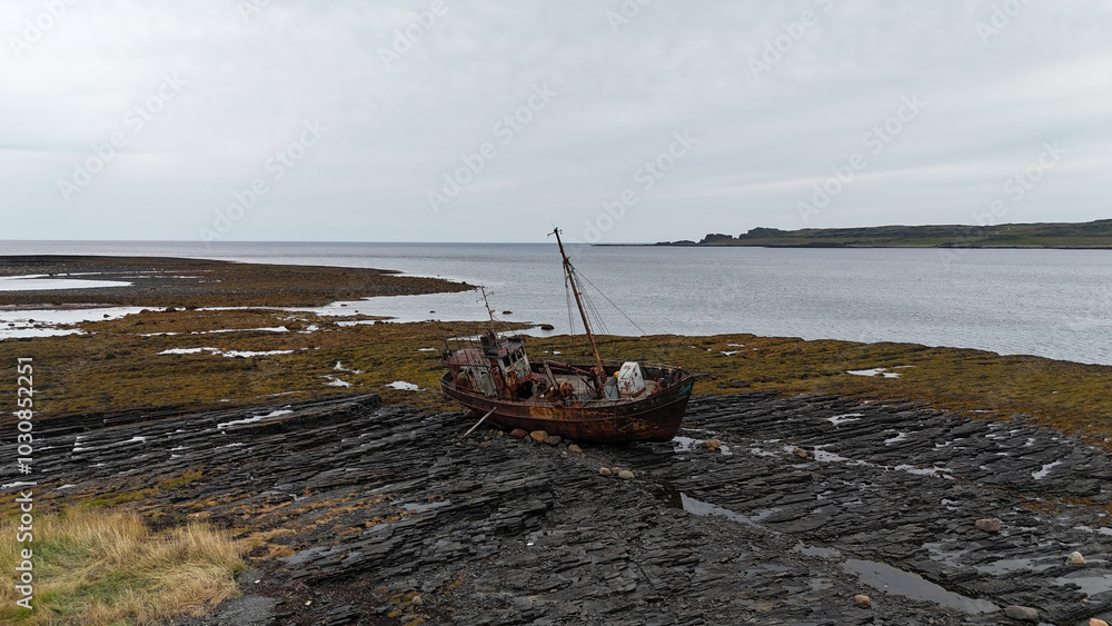 Abandoned fishing boat stranded on rocky shore during low tide near coastal landscape. Abandoned fishing boat stranded on rocky shore during low tide near coastal landscape.