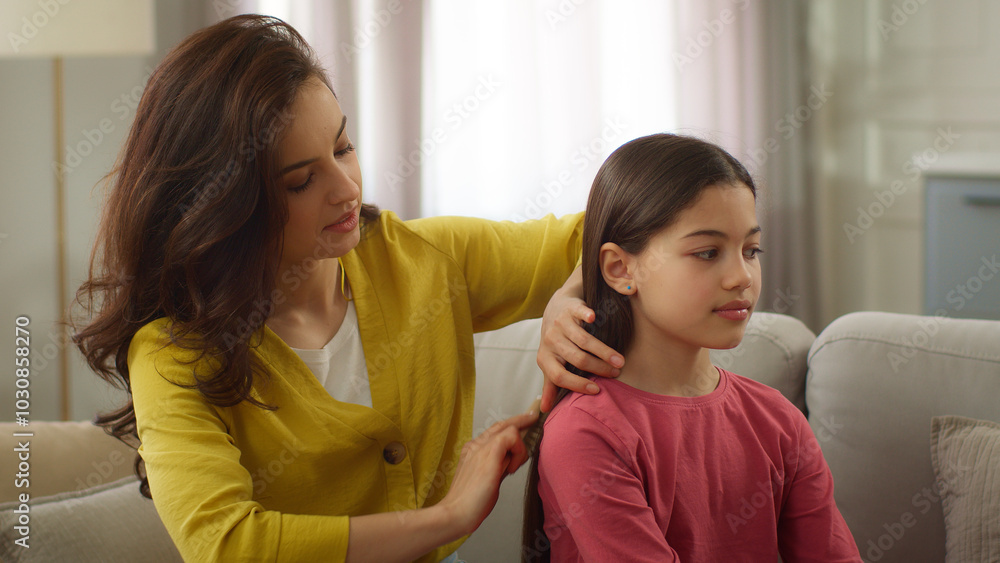 Smiling friendly family Caucasian sisters woman female mother sister babysitter combing brushing hair make hairstyle coiffure talking with little girl sibling child kid daughter sit living room home Smiling friendly family Caucasian sisters woman female mother sister babysitter combing brushing hair make hairstyle coiffure talking with little girl sibling child kid daughter sit living room home