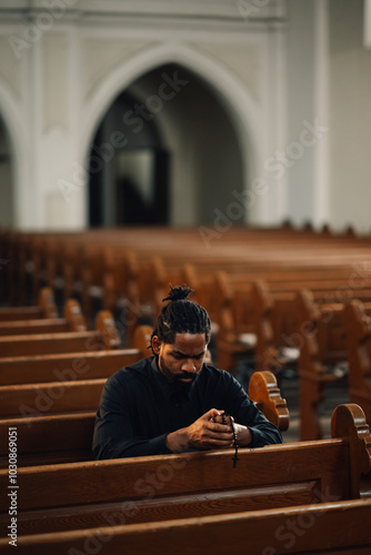 Fotografie Young man praying in church pew holding rosary beads