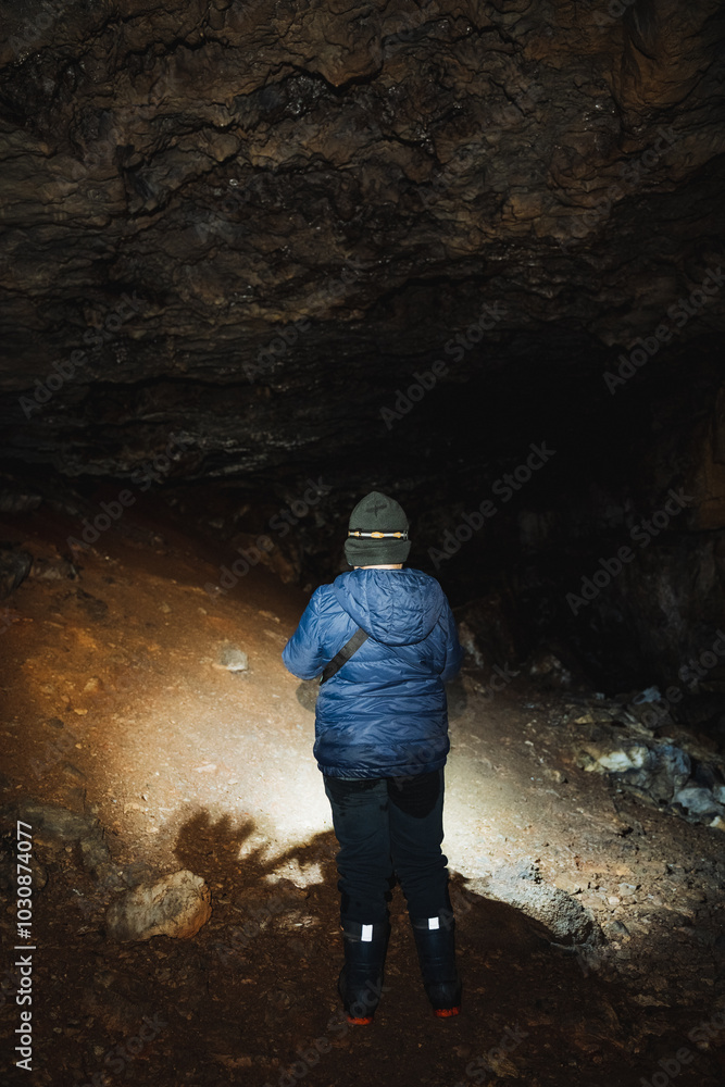 A solitary figure stands quietly in a dimly lit cave, holding a flashlight that casts light on the rocky walls and surrounding shadows, creating an intriguing and captivating air of mystery A solitary figure stands quietly in a dimly lit cave, holding a flashlight that casts light on the rocky walls and surrounding shadows, creating an intriguing and captivating air of mystery