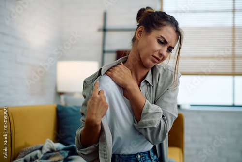 Photography Young woman feeling pain in her shoulder while sitting at home.