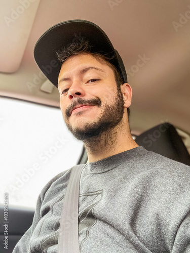 A person wearing a cap takes a selfie from inside a car. The colorful background outside the vehicle adds a lively contrast to the cozy interior, creating a vibrant yet casual atmosphere.