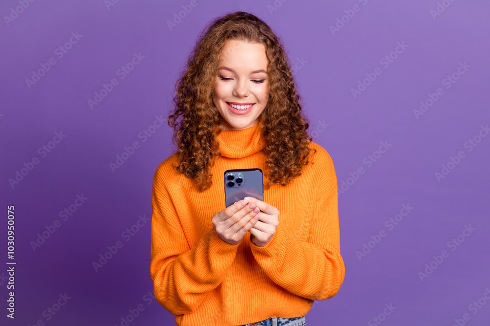 Portrait of pretty young girl use smart phone wear orange sweater isolated on purple color background