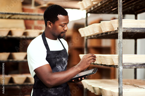 Black man, tablet and baker check stock, inventory or bread proofing basket on shelf. Technology, bakery and chef in factory for manufacturing, food production or quality inspection in small business photo