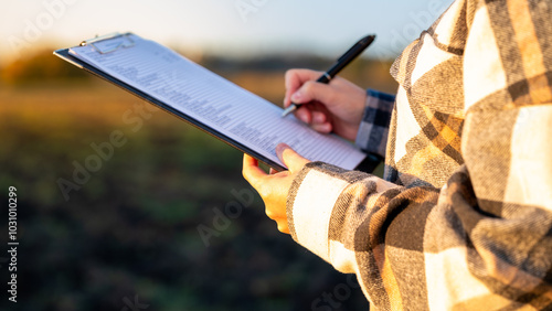 Person Holding a Clipboard While Recording Data in a Rural Setting During Sunset