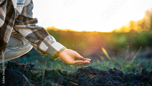 Фотография A Person in a Plaid Shirt Examines Soil While Kneeling in a Field at Sunset, Hig