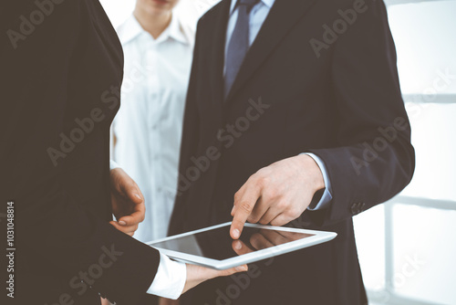 Businessman and woman using tablet computer for discussing questions in sunny office. Partners or colleagues at meeting. Cooperation concept