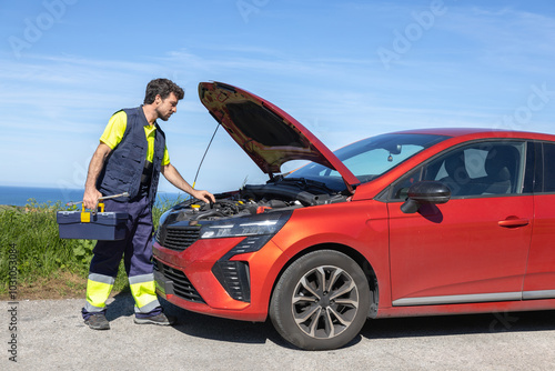 Young mechanic approaching broken vehicle on the road with reflective clothing, toolbox and cross wrench, broken engine, roadside assistance, insurance tow truck, car assistance