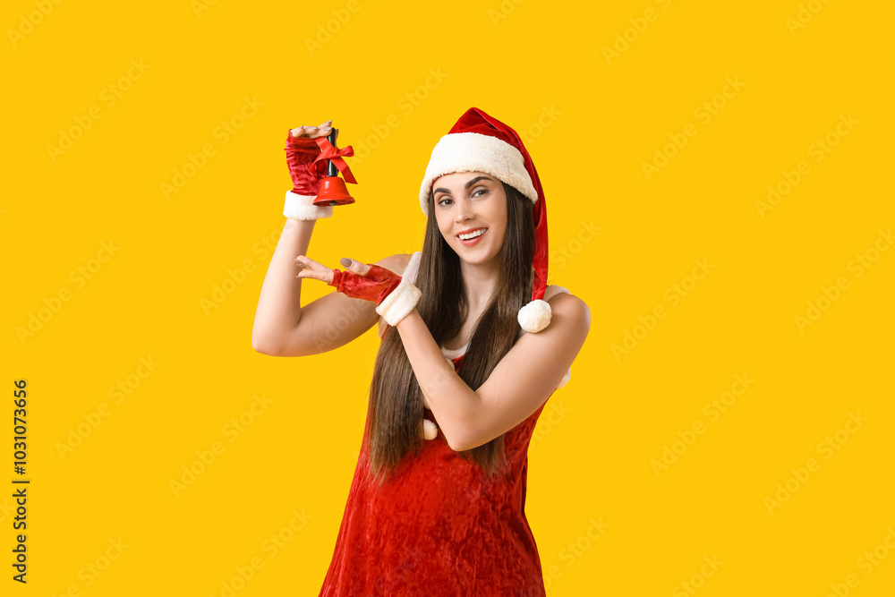 Young woman in Santa Claus costume with Christmas bell on yellow background Young woman in Santa Claus costume with Christmas bell on yellow background