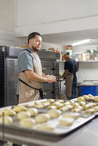 The focused baker stands before trays of dough, inspecting them thoroughly to guarantee top-quality pastries, indicating dedication to the craft of baking. photo