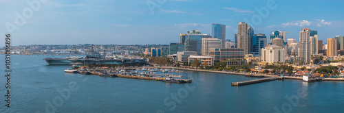 Aerial perspective of San Diego, California, showcasing the skyline, USS Midway Museum, bustling harbor, and rolling hills under a clear blue sky.