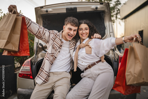 Photos young adult costumer couple with shopping bags sit in car trunk