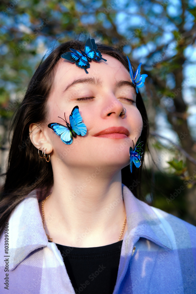 Face of young girl decorated with decorative blue butterflies in sunrays against green tree leaves Face of young girl decorated with decorative blue butterflies in sunrays against green tree leaves