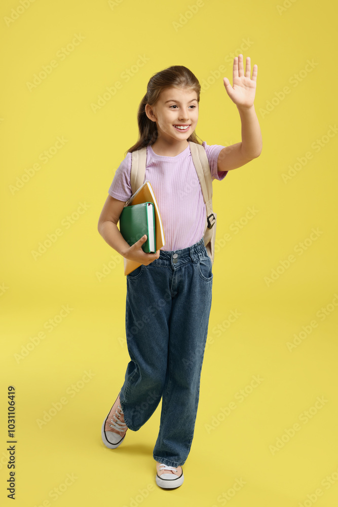 Girl with backpack and books waving on yellow background Girl with backpack and books waving on yellow background