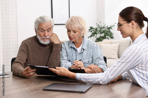 Pension plan. Senior couple consulting with insurance agent at wooden table indoors