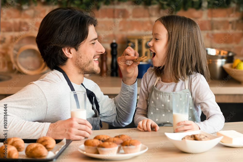 Healthy breakfast. Caring young dad feeding little daughter with homemade cookies and drinking milk together in kitchen, copy space Healthy breakfast. Caring young dad feeding little daughter with homemade cookies and drinking milk together in kitchen, copy space