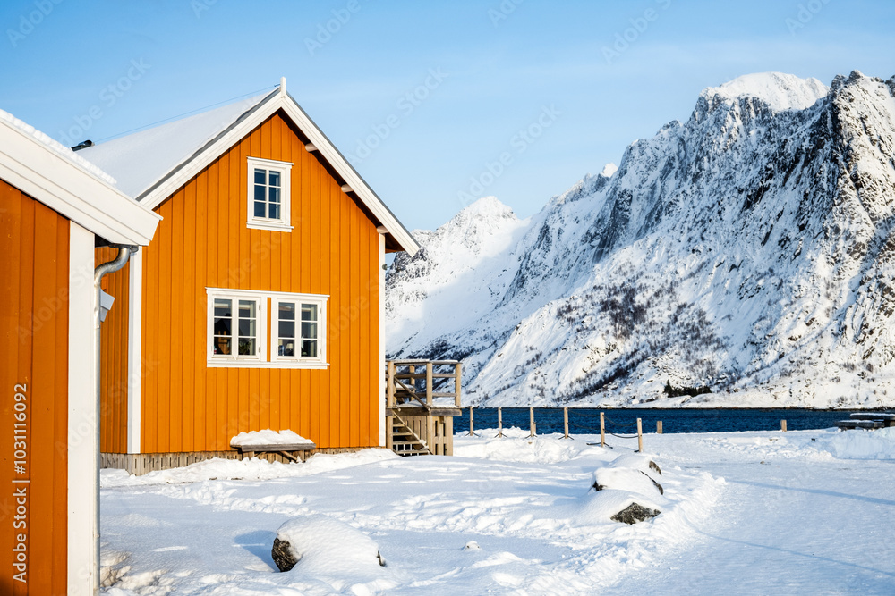 Fototapeta premium Traditional yellow rorbu house in Sakrisoy fishing village on Lofoten islands, Norway. Winter landscape with snowy mountains and Scandinavian cottage