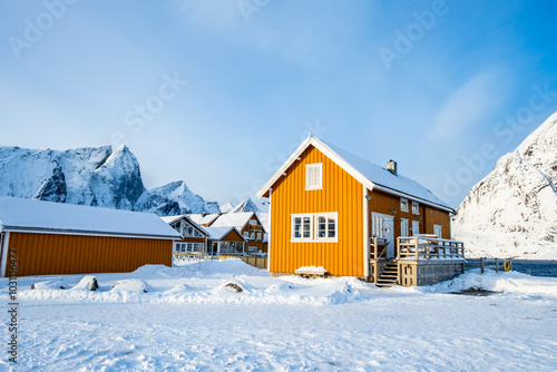 Traditional yellow rorbu house in Sakrisoy fishing village on Lofoten islands, Norway. Winter landscape with snowy mountains and Scandinavian cottage