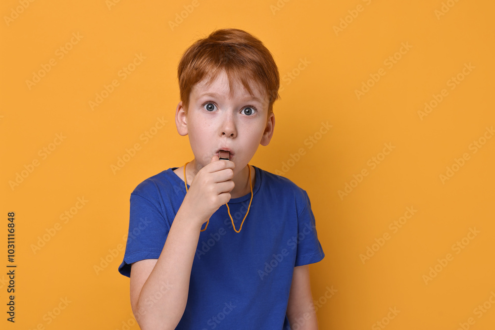 Little boy blowing whistle on orange background Little boy blowing whistle on orange background