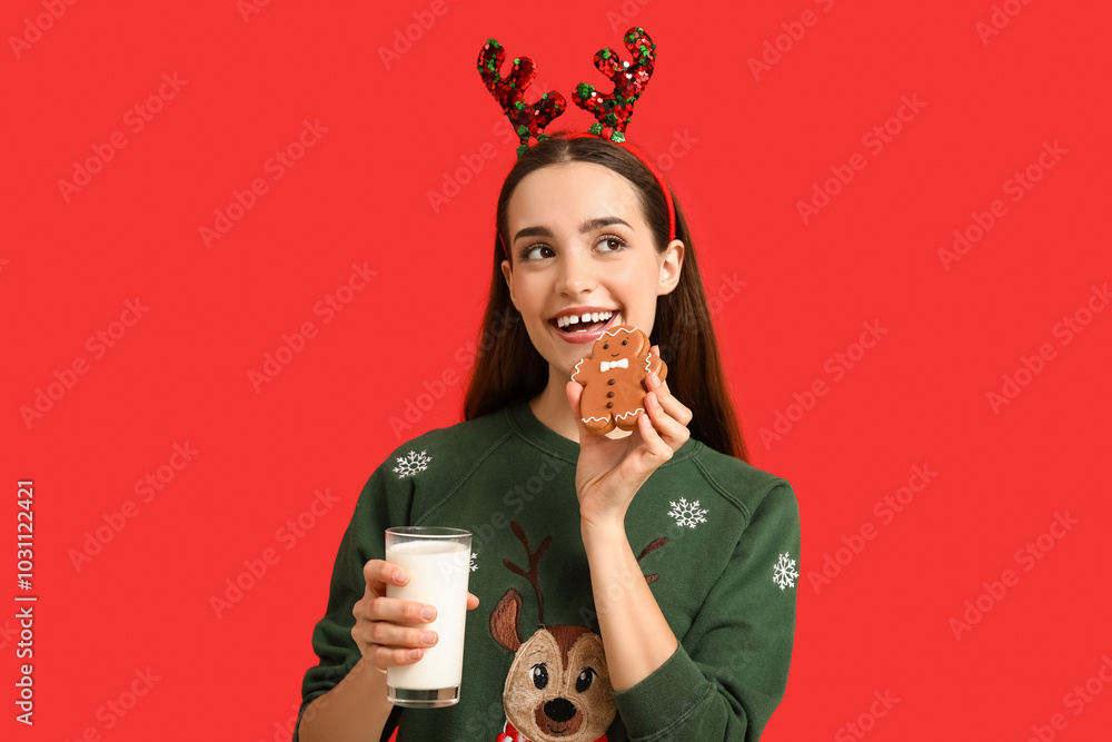Young woman with tasty Christmas gingerbread cookie and milk on red background Young woman with tasty Christmas gingerbread cookie and milk on red background