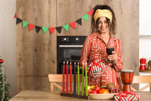 Young African-American woman with drink celebrating Kwanzaa in kitchen photo