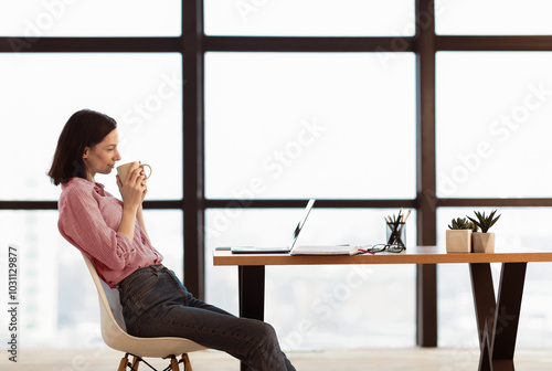 Morning Coffee. Side view of happy girl holding white mug, drinking hot beverage, using pc, free space