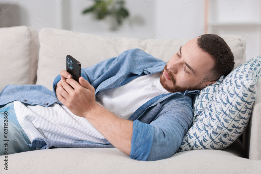 Handsome man looking at smartphone on sofa indoors Handsome man looking at smartphone on sofa indoors