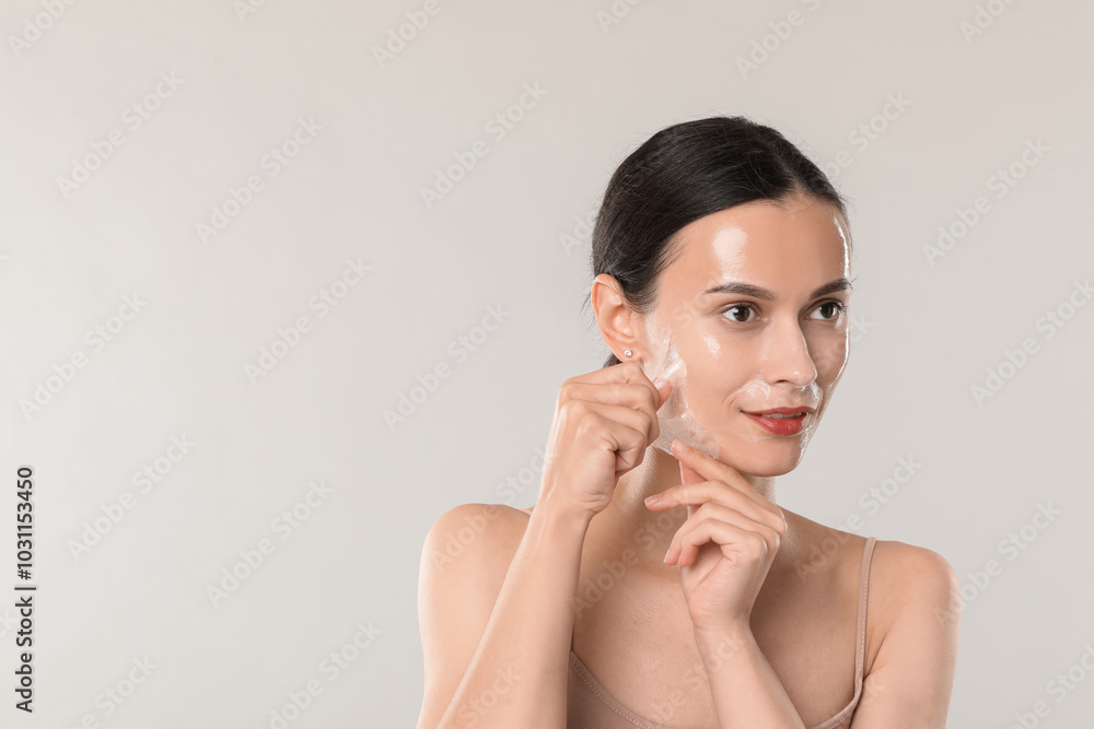 Smiling woman peeling off face mask on light grey background. Space for text Smiling woman peeling off face mask on light grey background. Space for text