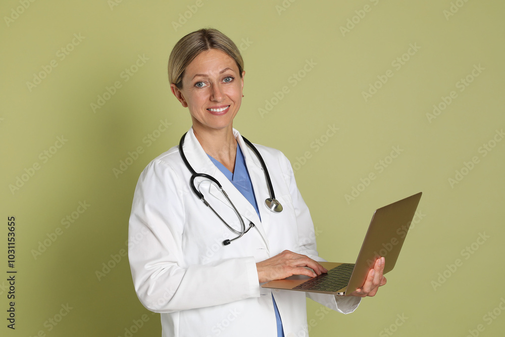 Doctor in medical uniform with stethoscope and laptop on light green background Doctor in medical uniform with stethoscope and laptop on light green background