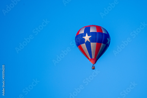 Hot air balloon in the distance in red blue and silver with 5 pointed star against a deep blue sky.