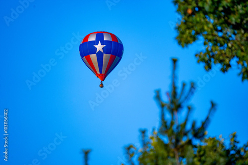 Hot air balloon in the distance in red blue and silver with 5 pointed star and trees in the foreground.