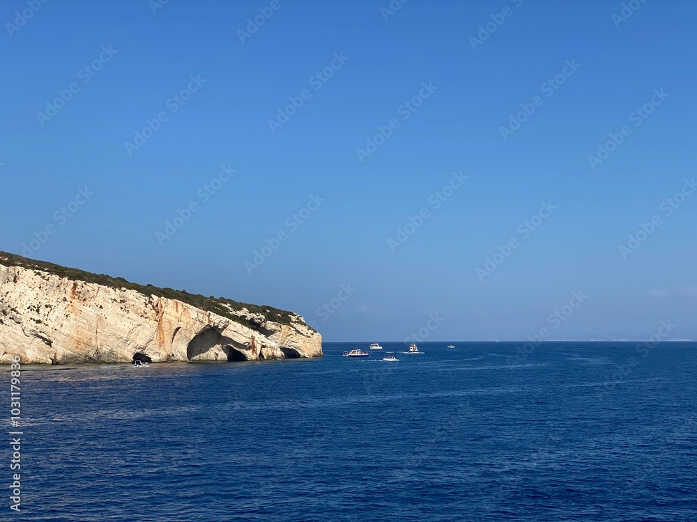 Coastal View with Boats Passing by Rocky Sea Caves Under Clear Blue Skies Coastal View with Boats Passing by Rocky Sea Caves Under Clear Blue Skies