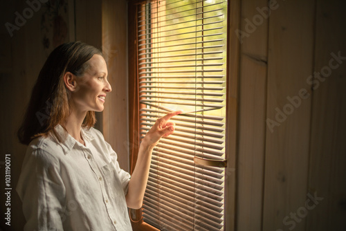 Good morning, happy smiling woman looking out bedroom window looking at the sunlight enjoying the warm sunshine, happy morning carefree lifestyle 