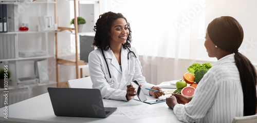 Cheerful dietologist showing female patient how to use mobile app for counting calories, clinic interior, free space photo