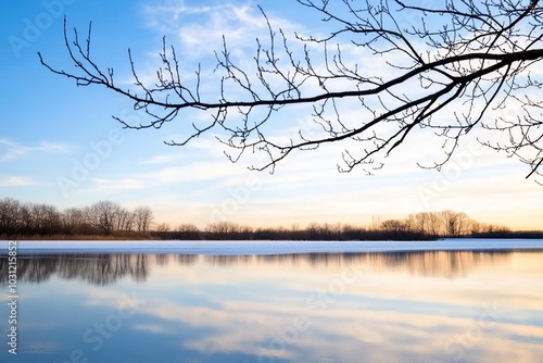 Serene landscape at sunset with tranquil water and bare branches.