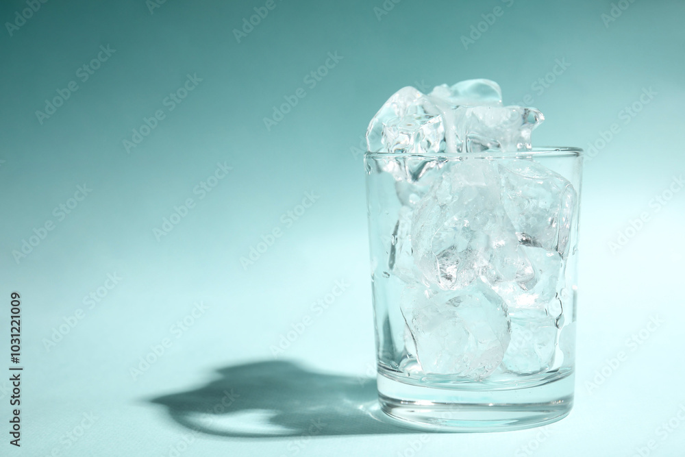 One glass with ice for refreshing drink on turquoise background. Space for text One glass with ice for refreshing drink on turquoise background. Space for text