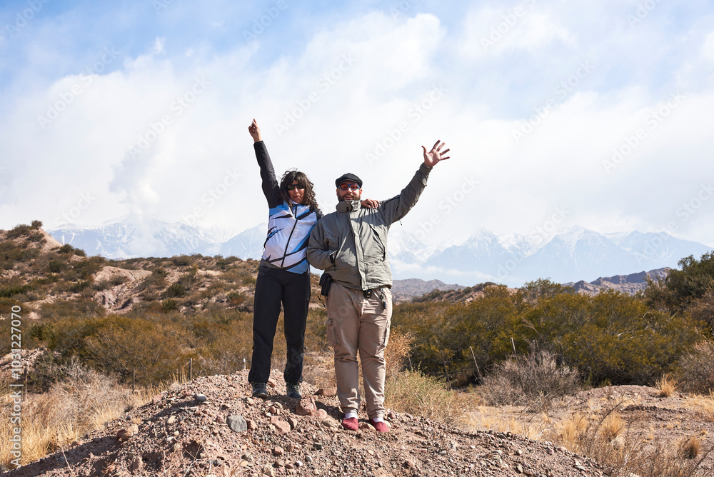 Obraz premium Couple of friends, man and woman, raising their arms, waving happily in a mountain landscape in Mendoza, Argentina.