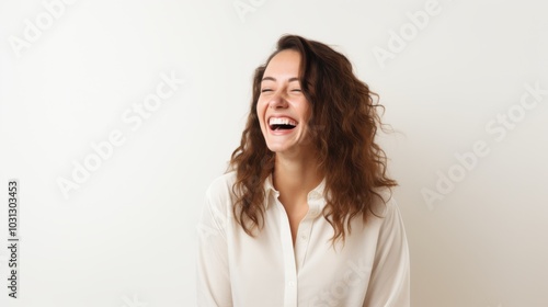 A joyful young woman stands against a light background, her laughter exuding warmth and positivity.