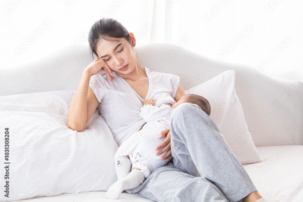 Asian Young mother holding her newborn child and breastfeeds baby, mom was exhausted from raising children. Adorable infant sucking a woman's breast after waking up in the morning. lady feeding baby. Asian Young mother holding her newborn child and breastfeeds baby, mom was exhausted from raising children. Adorable infant sucking a woman's breast after waking up in the morning. lady feeding baby.