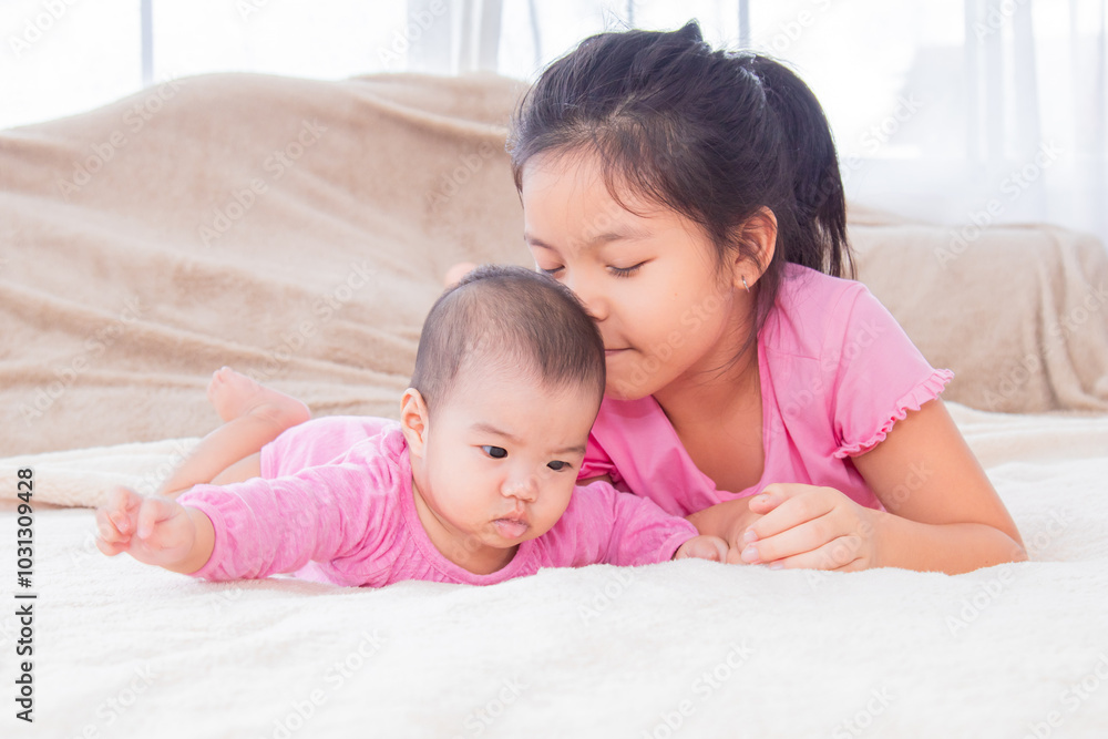 Asian happy cute big sister playing with adorable newborn baby girl in morning after waking up. elder sister teasing toddler while lying on bed together. Family relationships concept. Asian happy cute big sister playing with adorable newborn baby girl in morning after waking up. elder sister teasing toddler while lying on bed together. Family relationships concept.