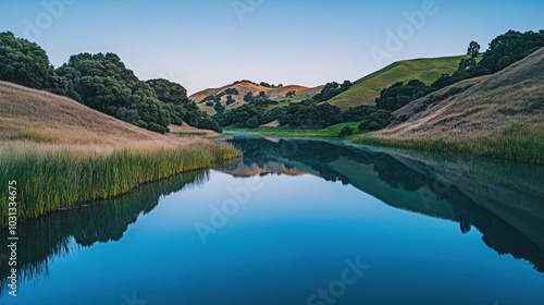 A serene lake surrounded by rolling hills reflecting the blue sky and lush greenery.