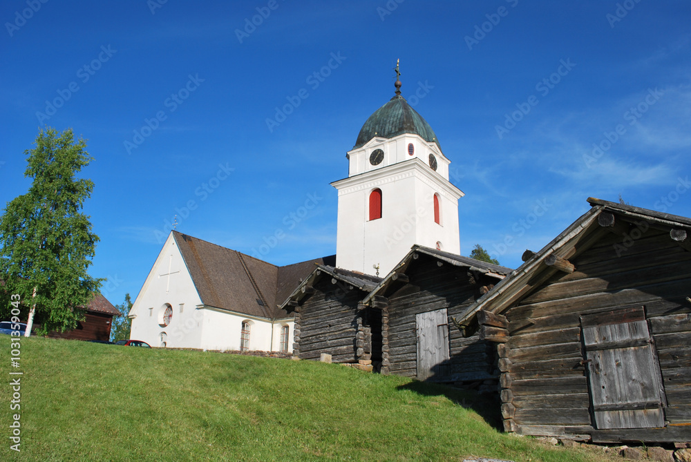 White scandinavian church with wooden sheds amidst clear blue sky in a small village town in Sweden White scandinavian church with wooden sheds amidst clear blue sky in a small village town in Sweden