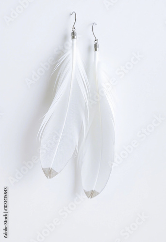 Close-up of two delicate, white feather earrings with gold hooks, set against a simple, white background. Ideal for concepts of elegance, simplicity, and minimalism.