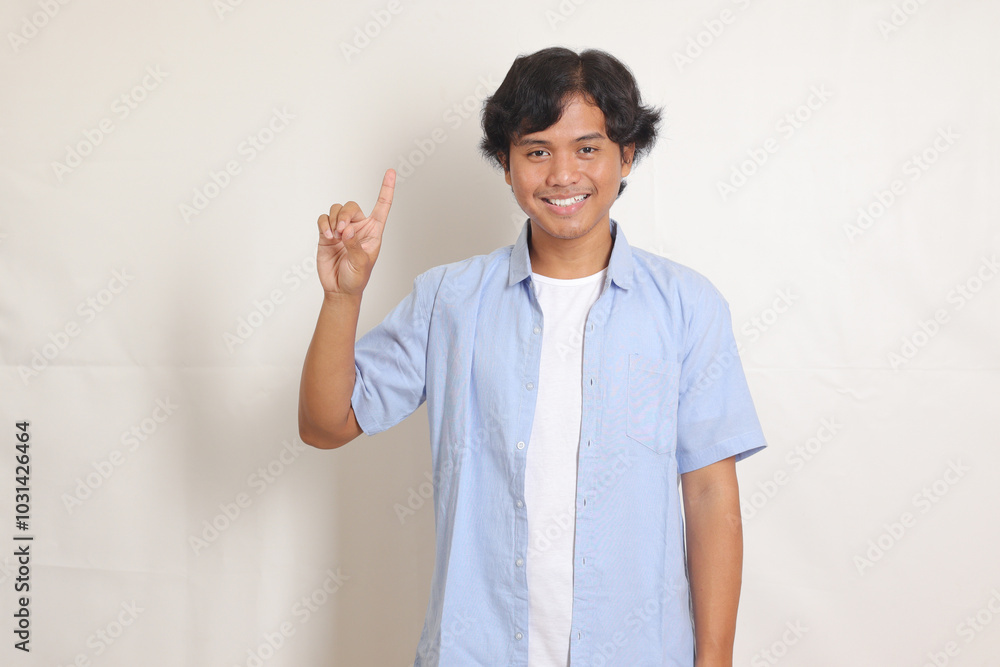 Portrait of excited Asian man in blue shirt counting one with finger. Reminder concept. Isolated image on white background Portrait of excited Asian man in blue shirt counting one with finger. Reminder concept. Isolated image on white background