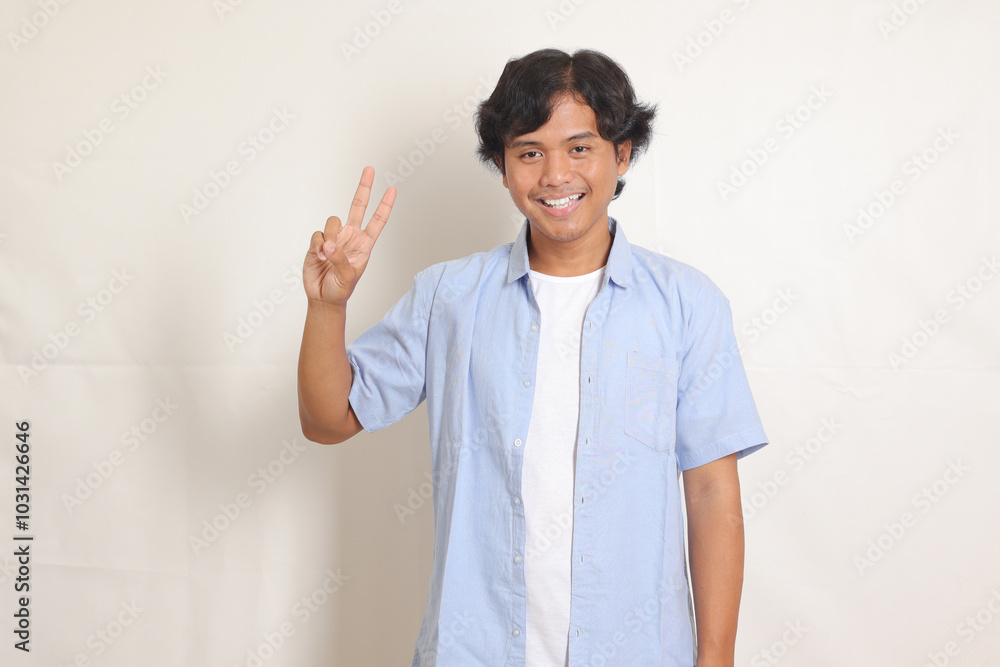 Portrait of excited Asian man in blue shirt counting two with finger. Reminder concept. Isolated image on white background Portrait of excited Asian man in blue shirt counting two with finger. Reminder concept. Isolated image on white background