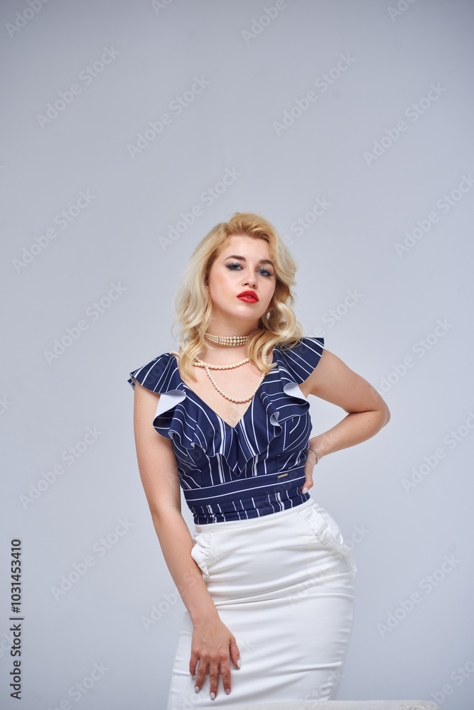 Beautiful girl with blond hair in blue and white dress posing in studio on white background. She is wearing pink shoes and red necklace. Beautiful girl with blond hair in blue and white dress posing in studio on white background. She is wearing pink shoes and red necklace.
