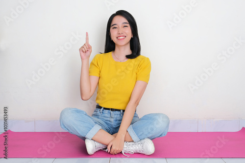 A woman sitting cross legged and pointing up with happy expression photo