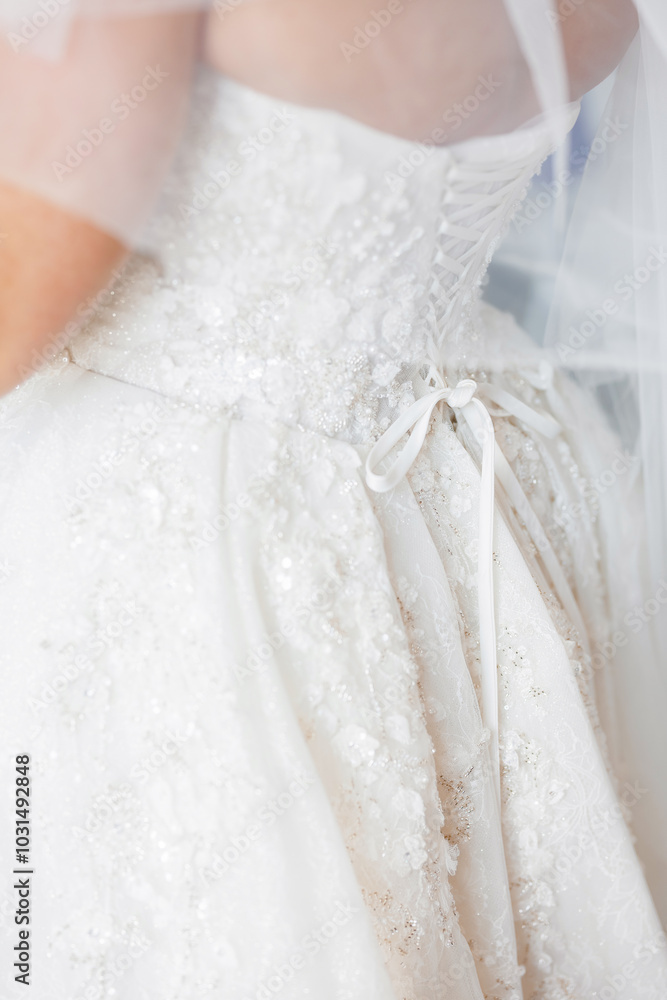 Bride in white wedding dress close-up view from the back. Beautiful wedding dress of the bride tied at the back with a lace. Preparation of the bride for the wedding ceremony Bride in white wedding dress close-up view from the back. Beautiful wedding dress of the bride tied at the back with a lace. Preparation of the bride for the wedding ceremony