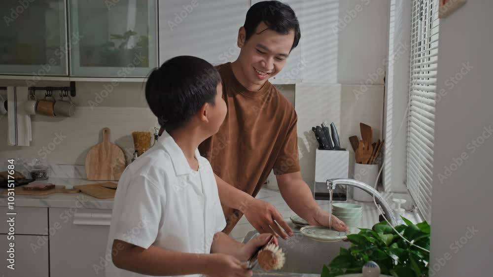 Tilt down shot of young Asian father and teenage son rinsing dishes at kitchen sink Tilt down shot of young Asian father and teenage son rinsing dishes at kitchen sink