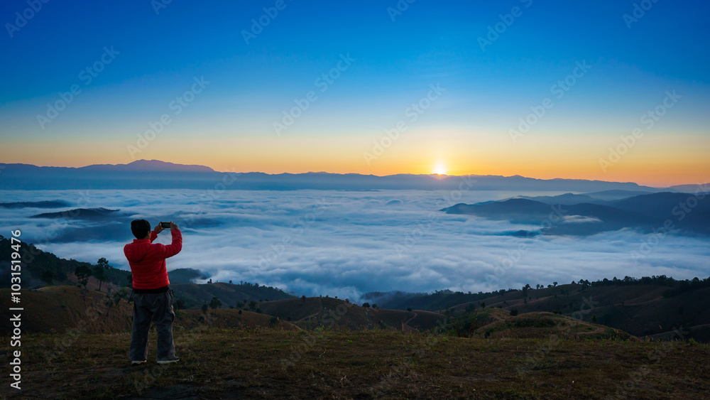 Asian man takes a photo of the beautiful natural scenery of the sea of mist in the morning at Doi Ba Lu Kho Mountain View Point, Mae Chaem, Chiang Mai, Northern Thailand. Asian man takes a photo of the beautiful natural scenery of the sea of mist in the morning at Doi Ba Lu Kho Mountain View Point, Mae Chaem, Chiang Mai, Northern Thailand.